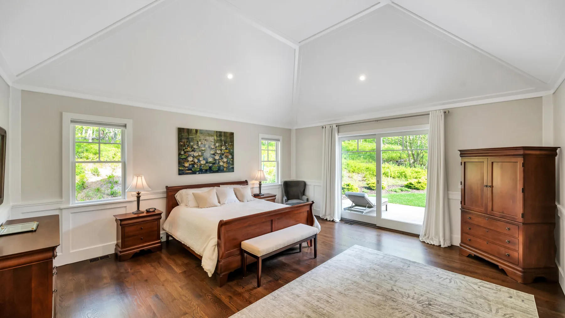 A bright bedroom with a bed, wooden furnishings, and large glass doors.