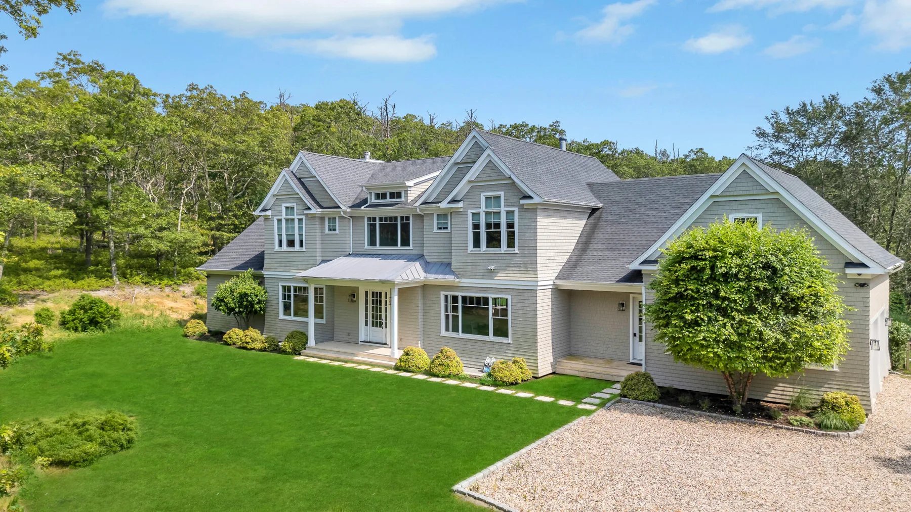 A large house with gray roofs stands beside a broad green lawn and gravel driveway.