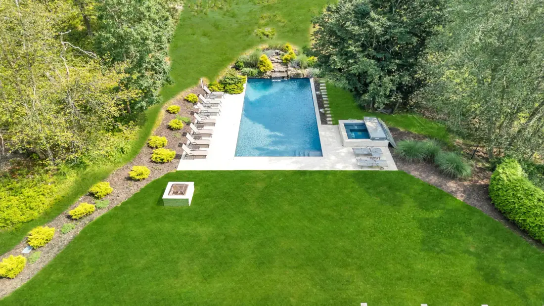 An outdoor swimming pool sits beside a broad lawn and surrounding trees.