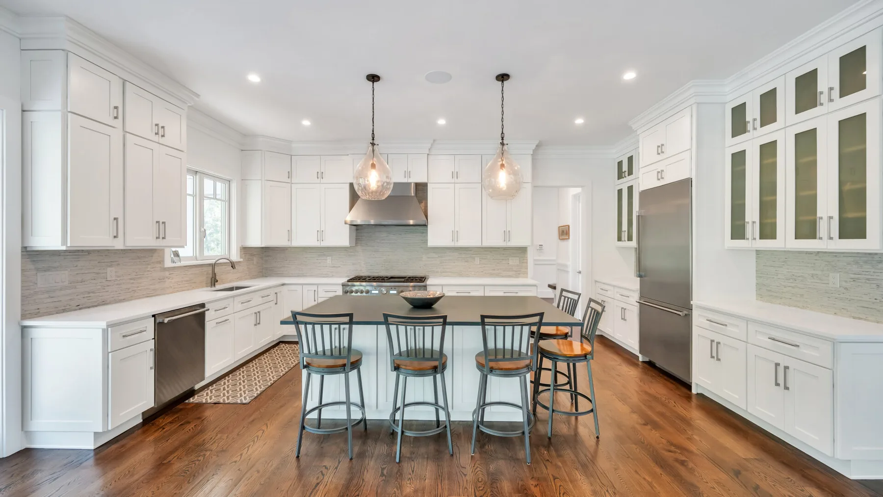A bright kitchen with a central island and seating beneath two pendant lights.