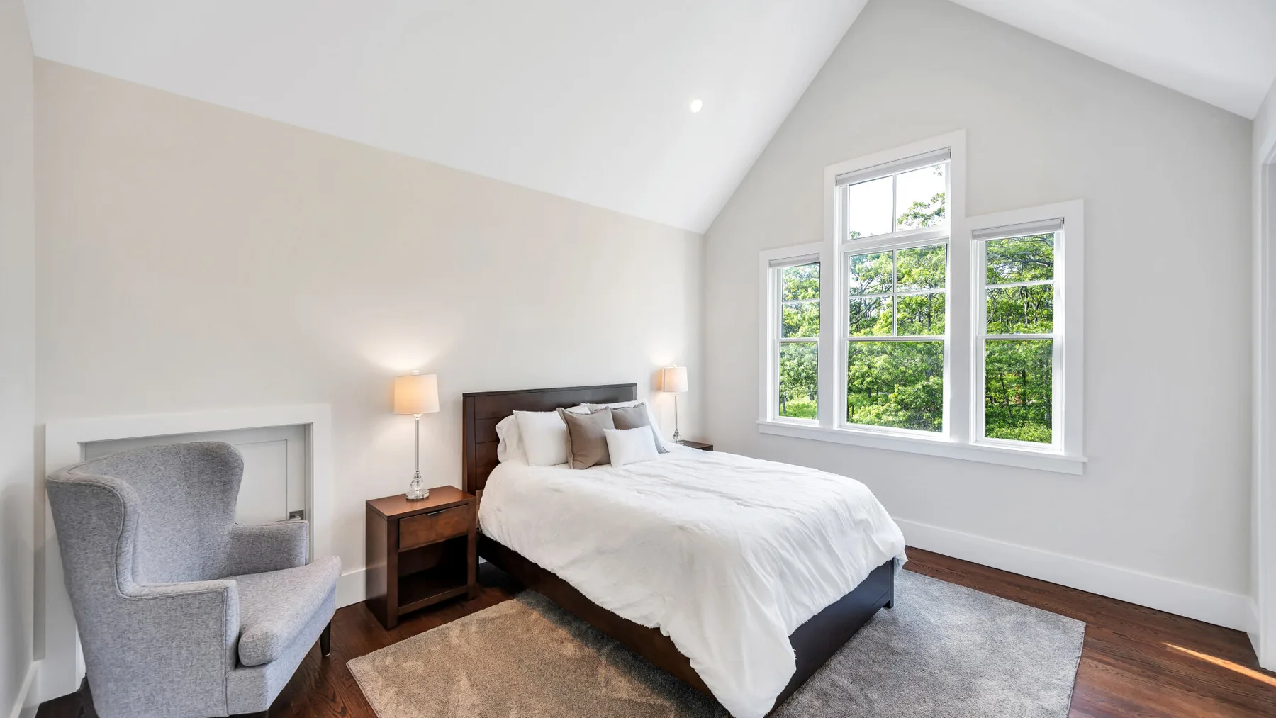A bright bedroom with a bed, bedside table, and large windows.