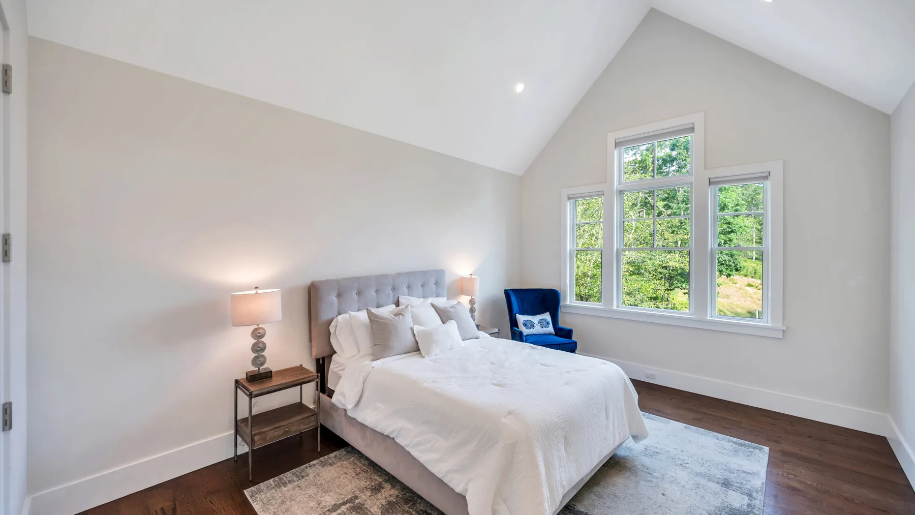 A bright bedroom with a neatly made bed beside large windows.