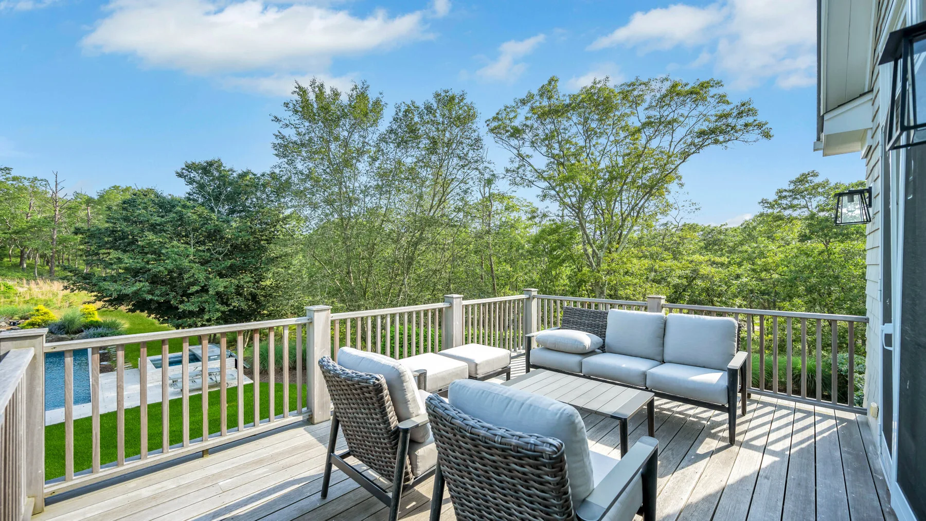 An outdoor deck with seating overlooks a green, tree-filled landscape.