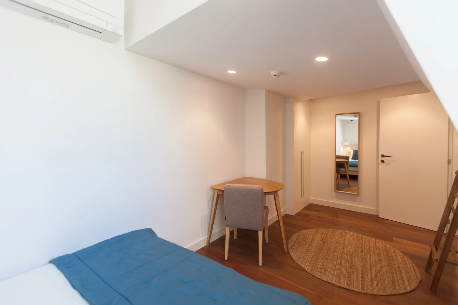 A bedroom with a bed, desk, and oval rug on a wood floor.