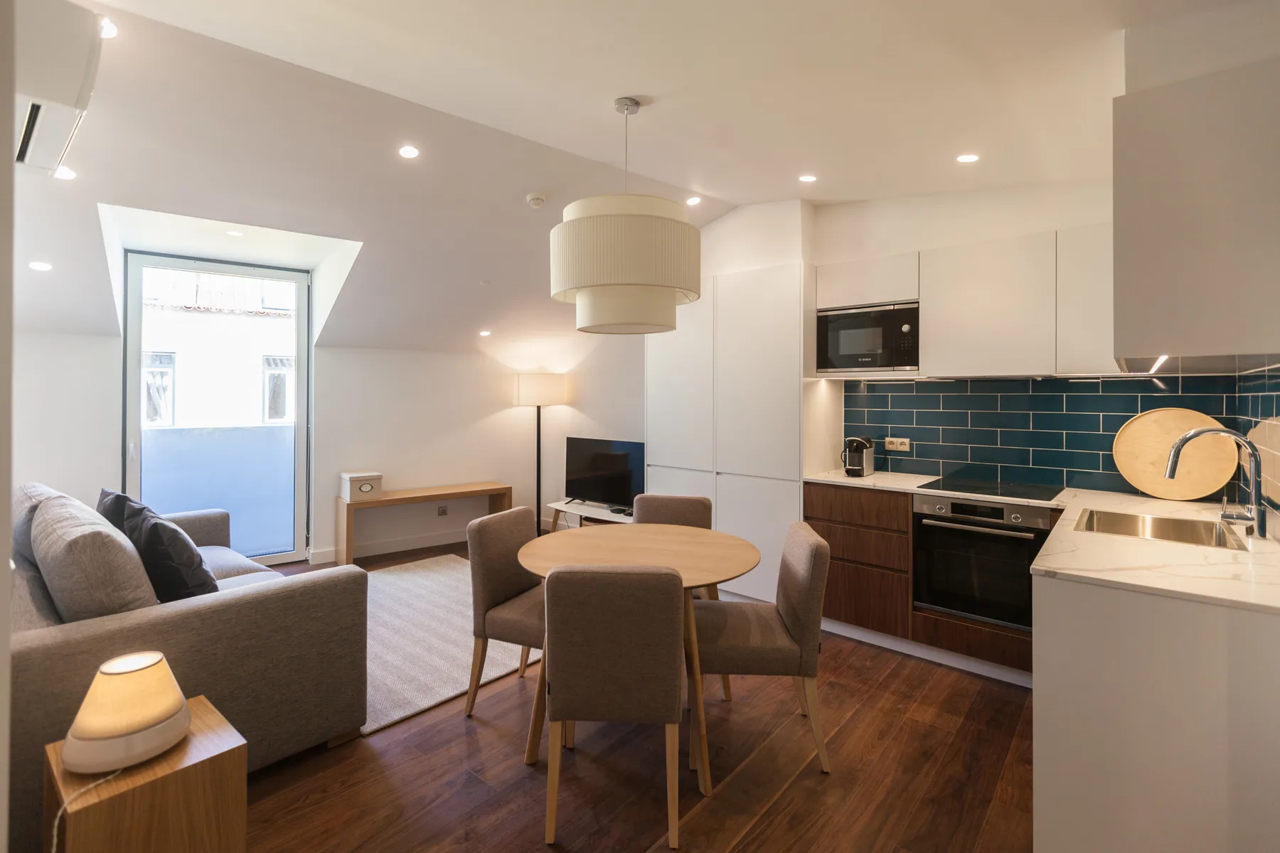 An open-plan living and dining area with a kitchen and blue tile backsplash.