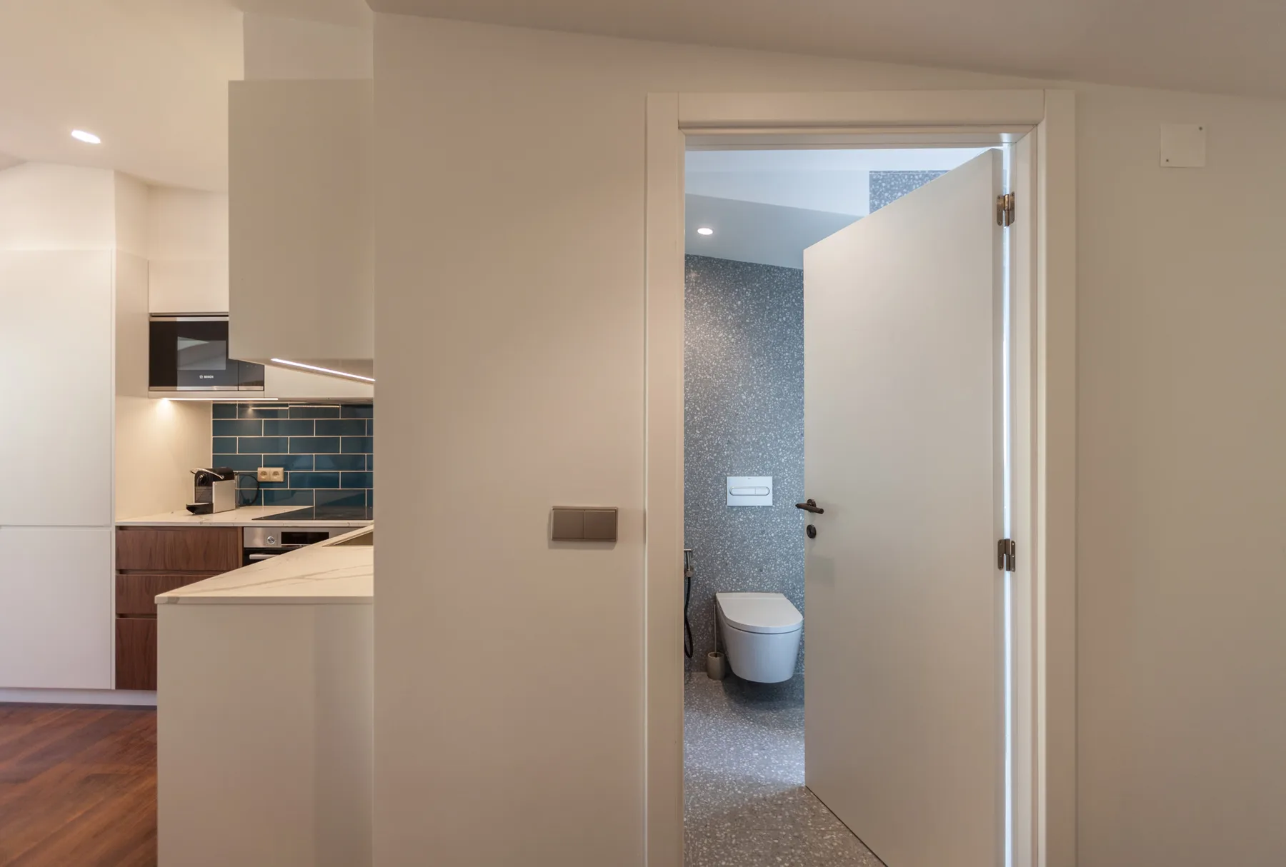 A bathroom with a toilet is visible through an open doorway beside a kitchen.