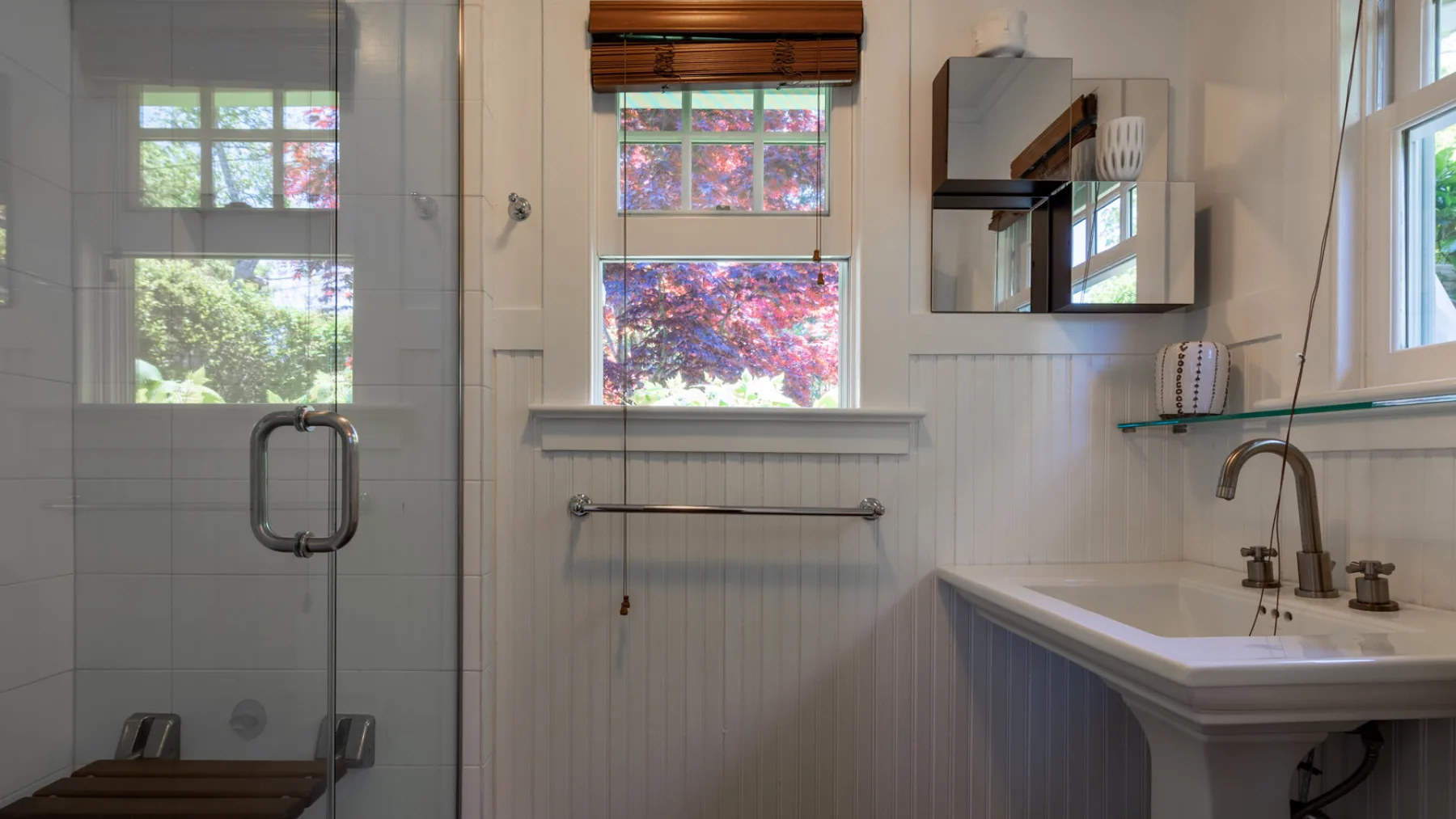 A bright bathroom with a glass shower, bathtub, and windows overlooking greenery.