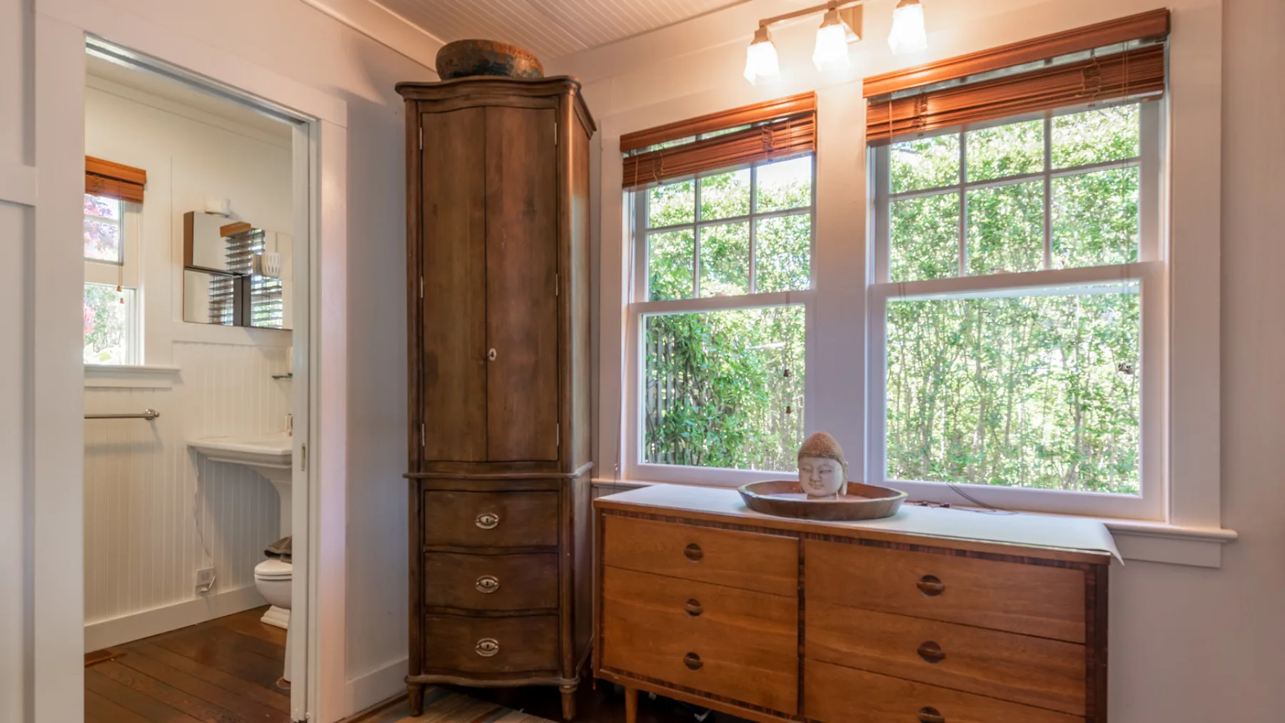 A bright bathroom with a wooden vanity beneath two large windows.