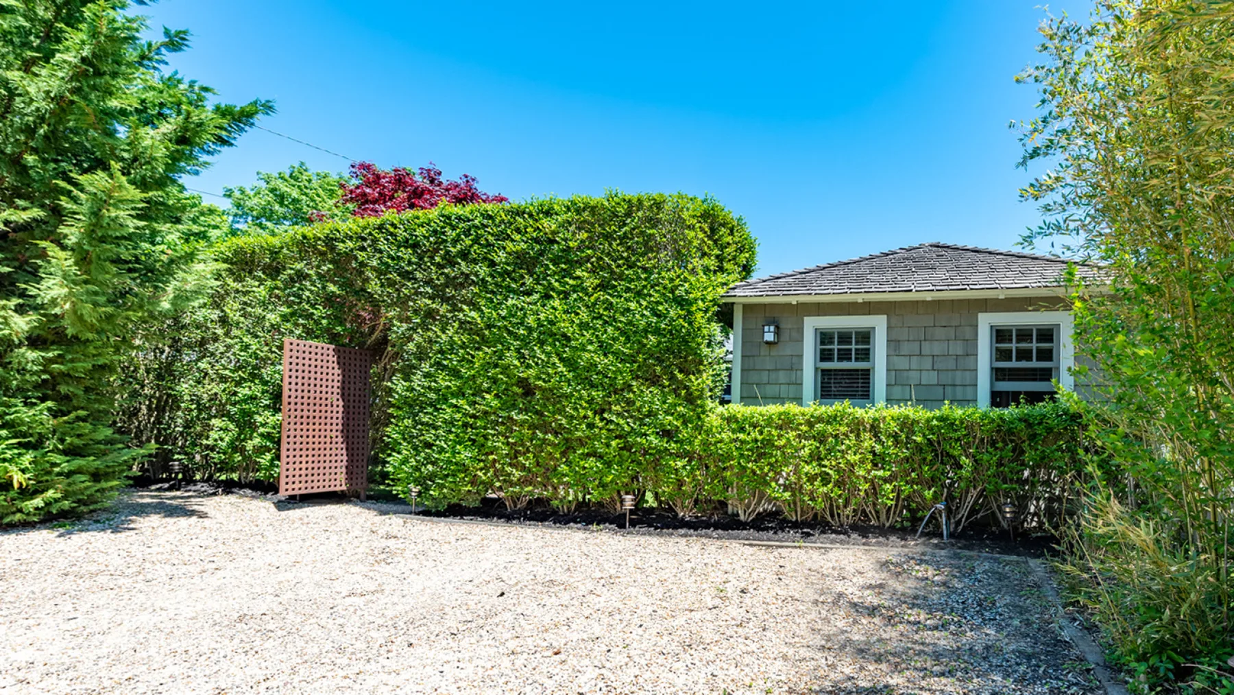 A gravel driveway bordered by tall hedges leads toward a house.