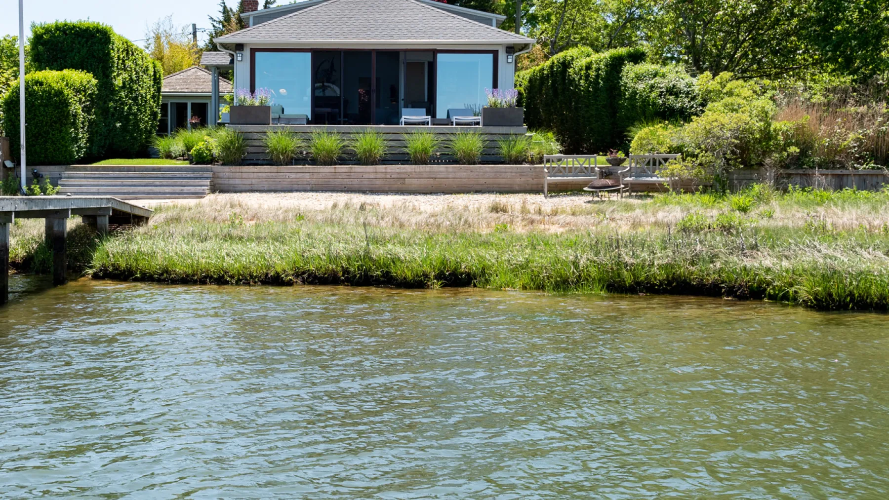 A modern house sits beside a calm waterway, with a landscaped garden in front.