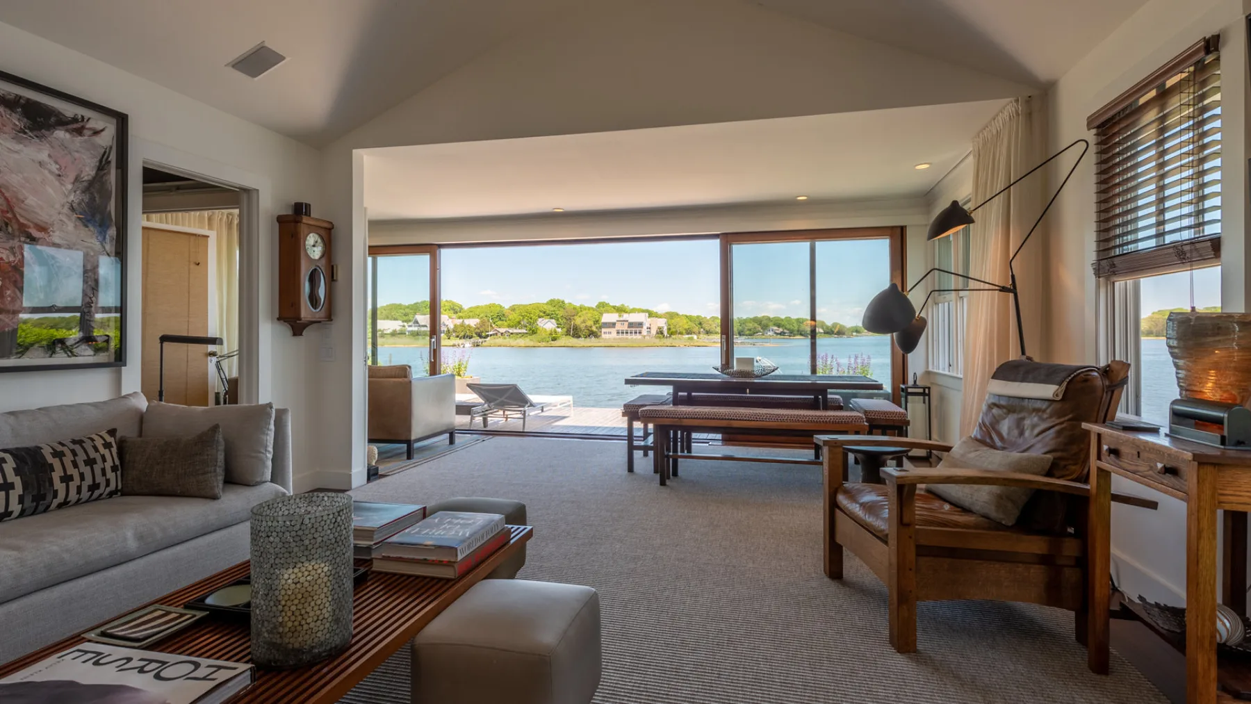 A bright living room opens onto a waterfront view, with seating and a low table.