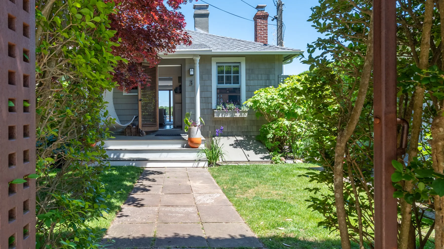 A paved path leads through a garden toward a small house.