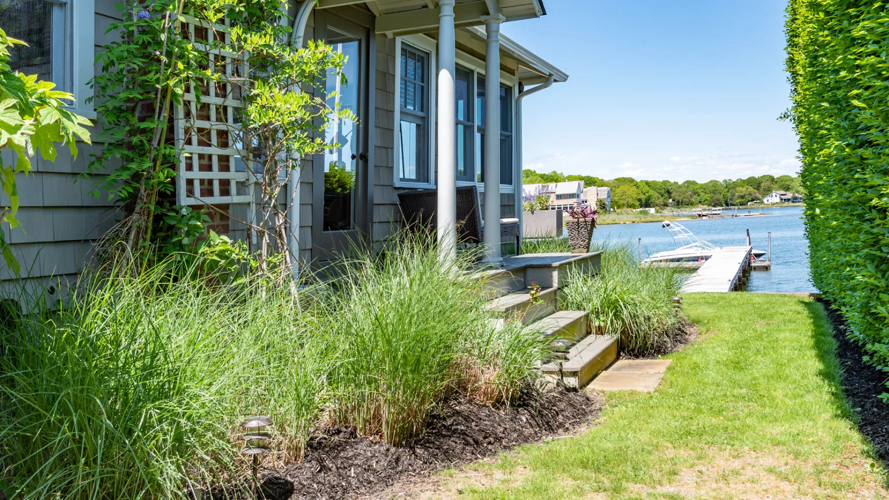 A lakeside house beside a grassy yard, with a small dock extending into the water.