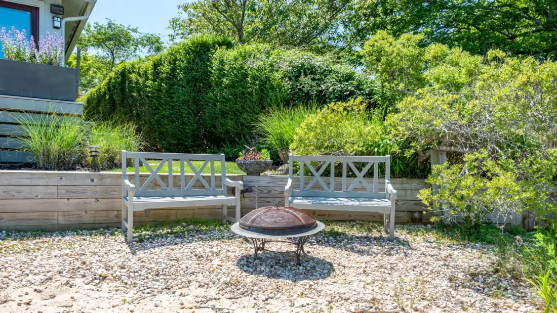 An outdoor seating area with two benches and a low round table in a leafy garden.