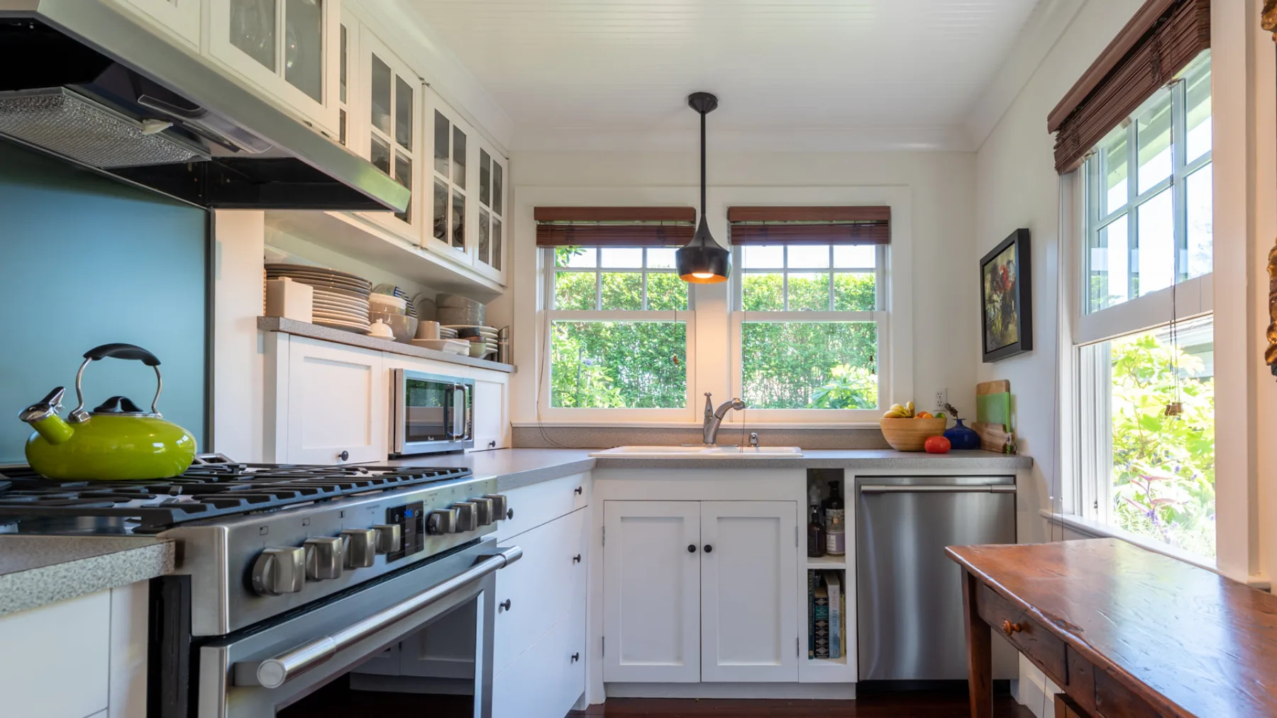 A bright kitchen with white cabinetry, a cooking range, and windows overlooking greenery.