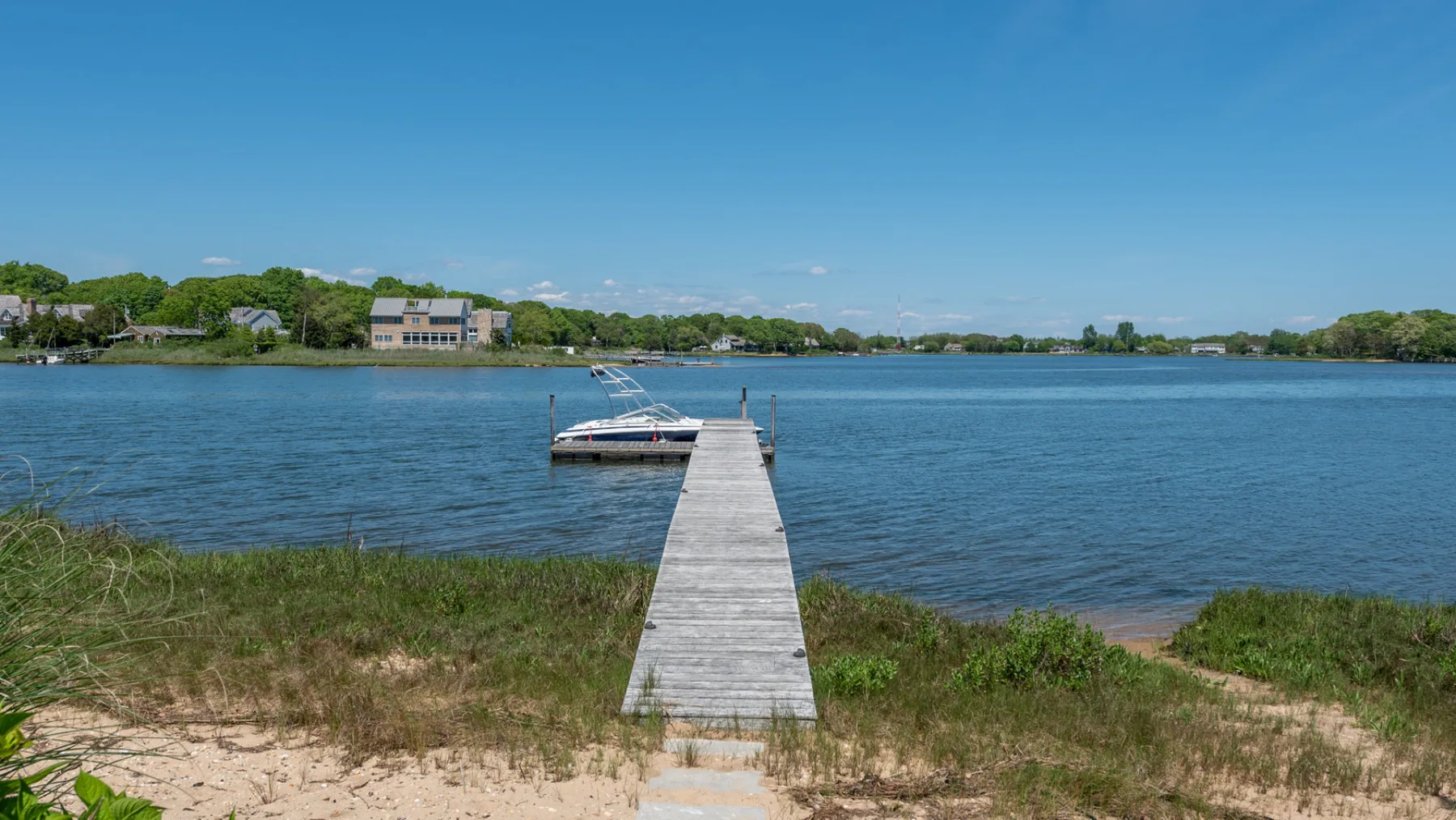 A wooden dock extends from a grassy shoreline into a calm lake.