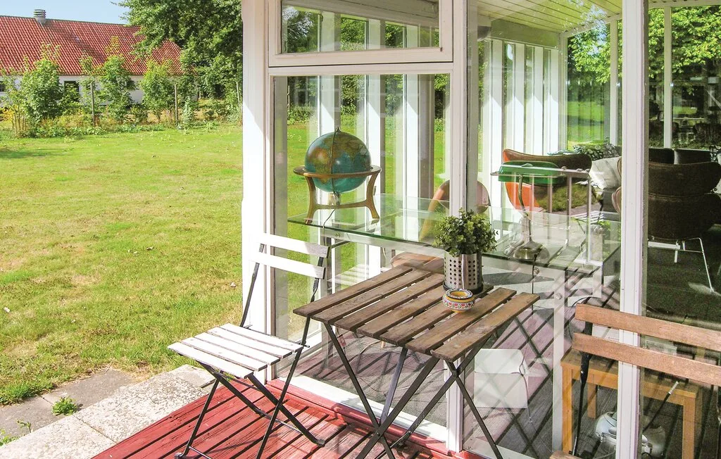 Un patio acristalado con una mesa de madera y sillas da a un jardín con césped.