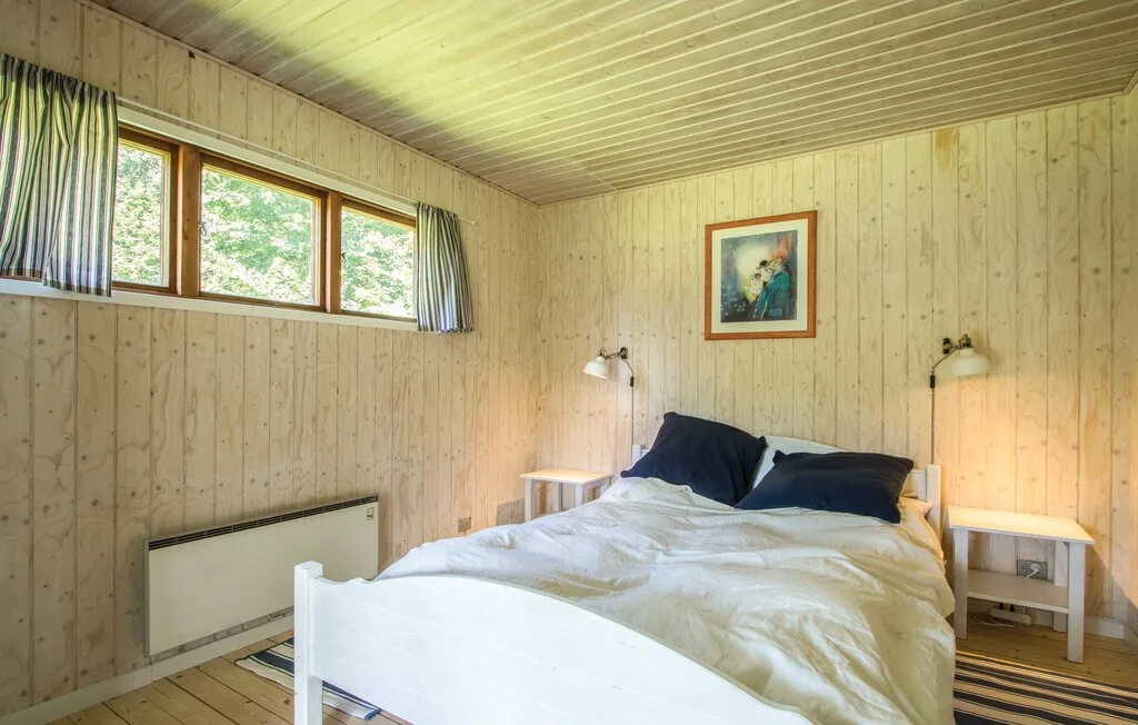 Un dormitorio con una cama, mesitas de noche y una ventana alta.