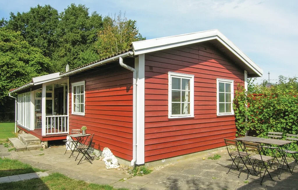 Una casa de revestimiento rojo con ventanas de marco blanco y asientos al aire libre en un patio pavimentado.