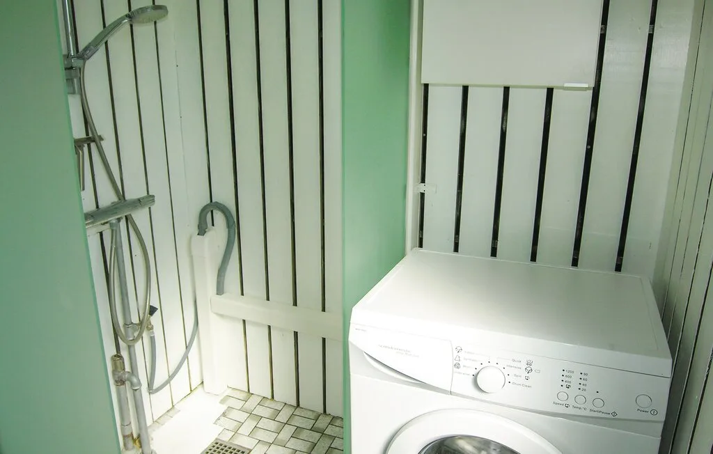 Una pequeña zona de lavandería con una lavadora junto a una ducha.