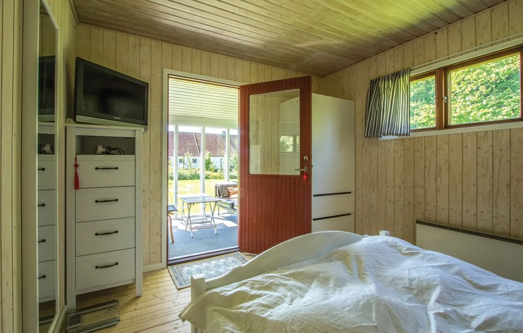 Dormitorio revestido de madera con una cama y una puerta abierta al patio.
