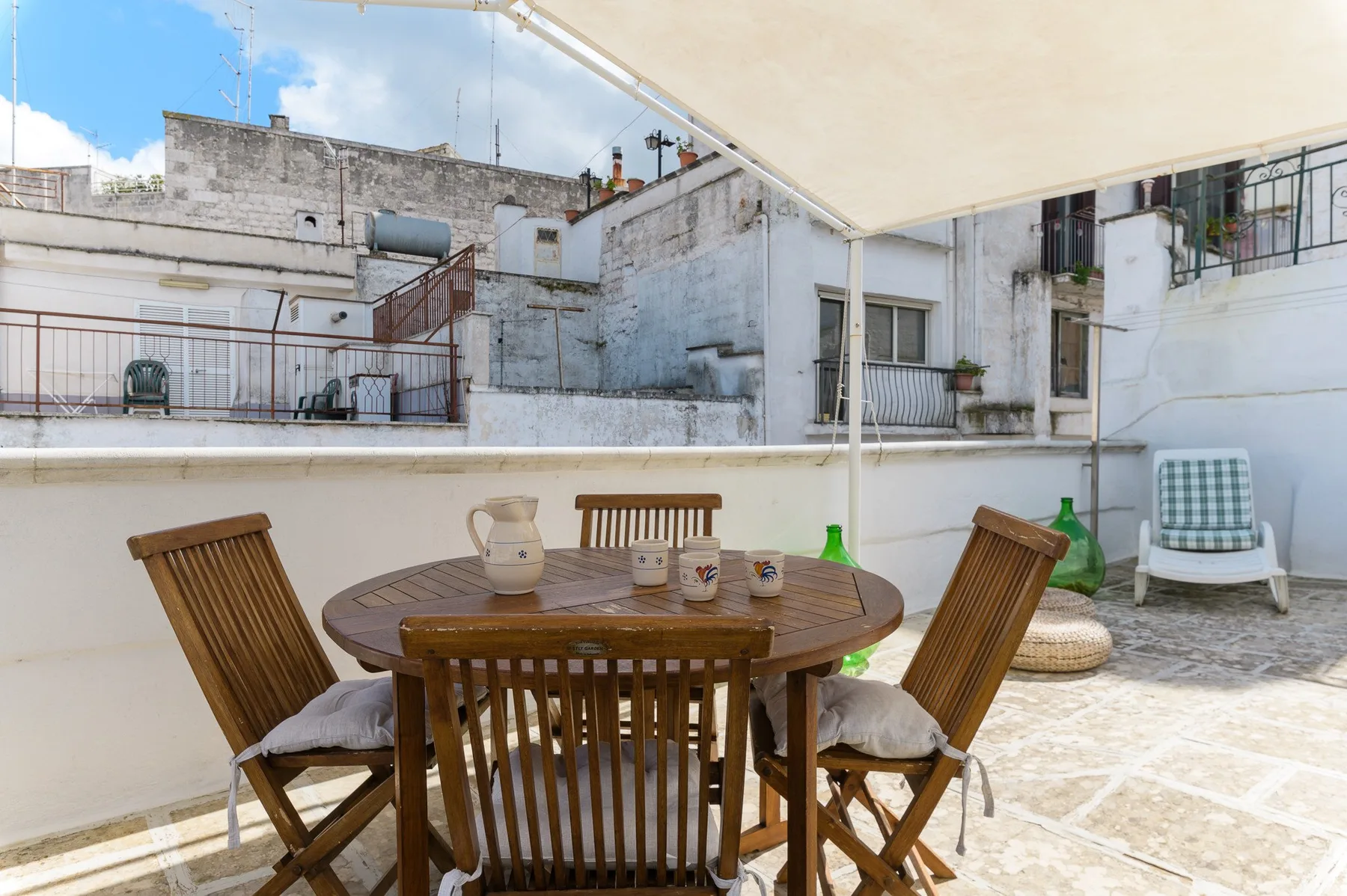 Una terraza en la azotea con una mesa de comedor de madera y sillas bajo un toldo.