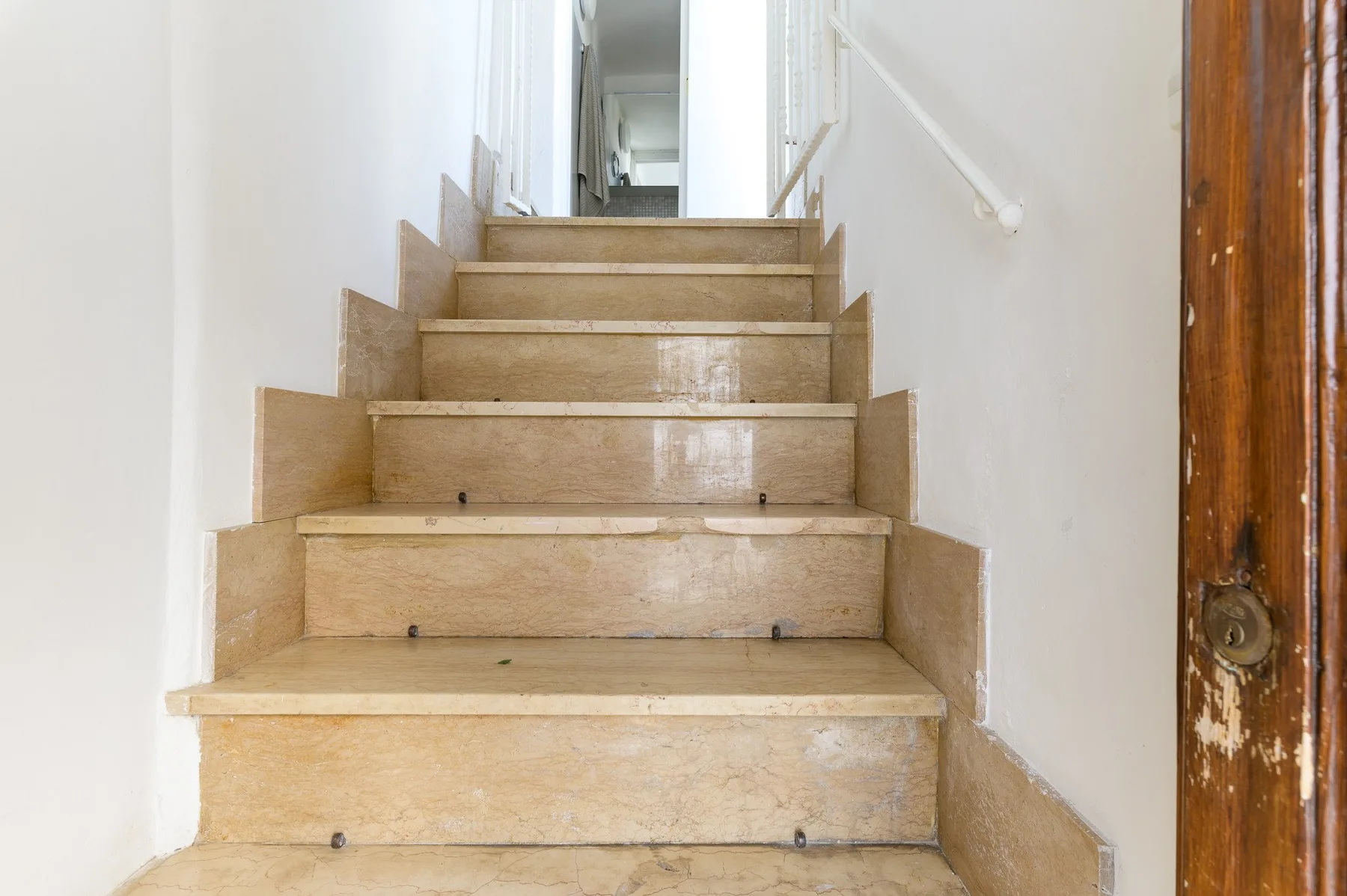 Una escalera interior con peldaños claros y una barandilla blanca.