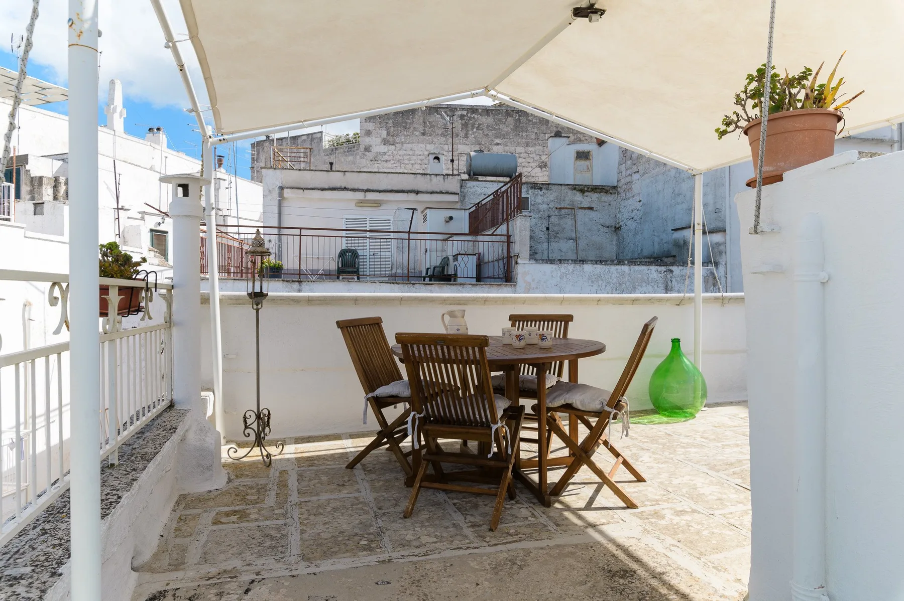 Una terraza soleada tiene una mesa de comedor de madera y sillas bajo un toldo.