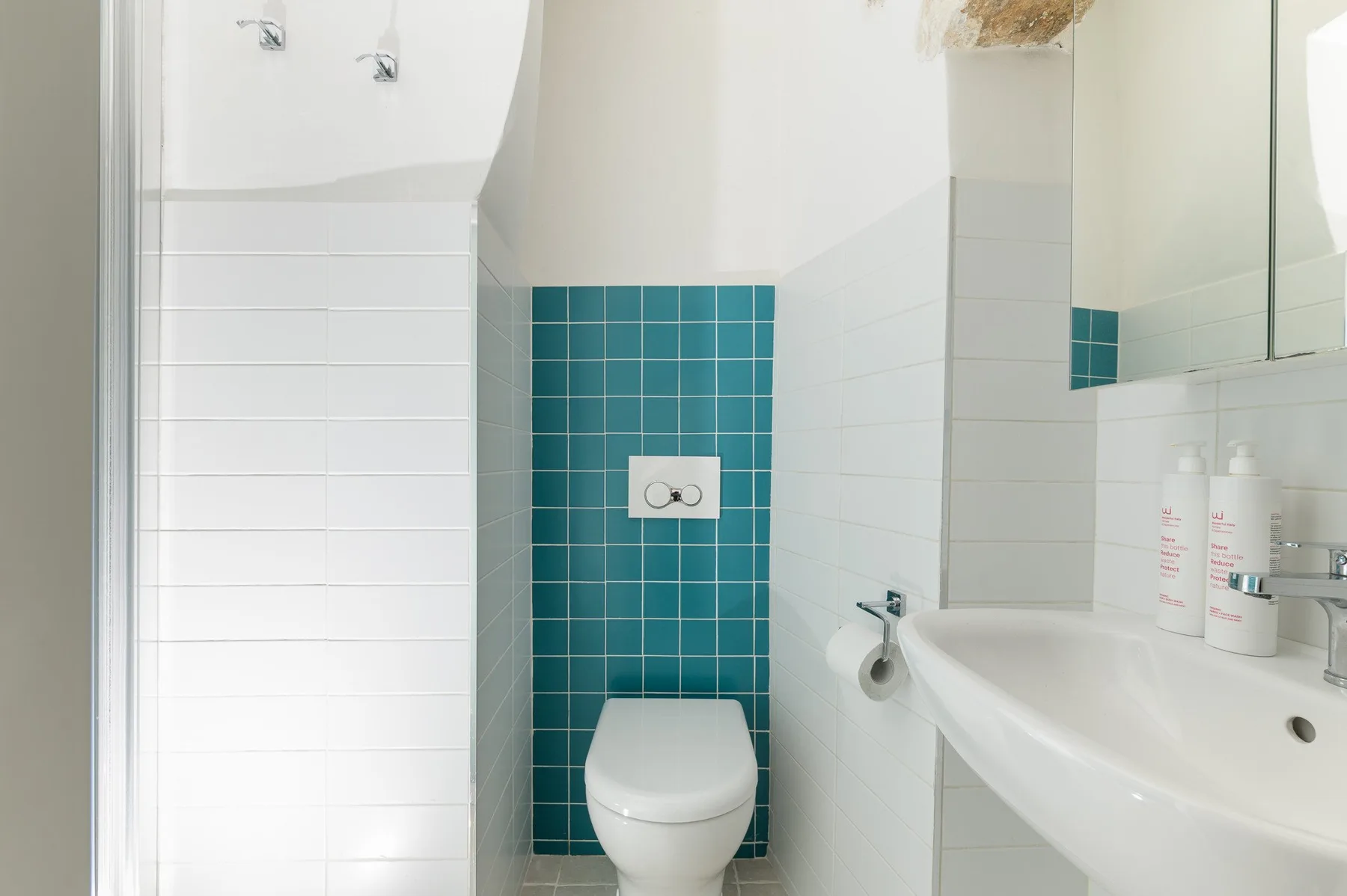 Un baño alicatado con inodoro, lavabo y accesorios de ducha en la pared.