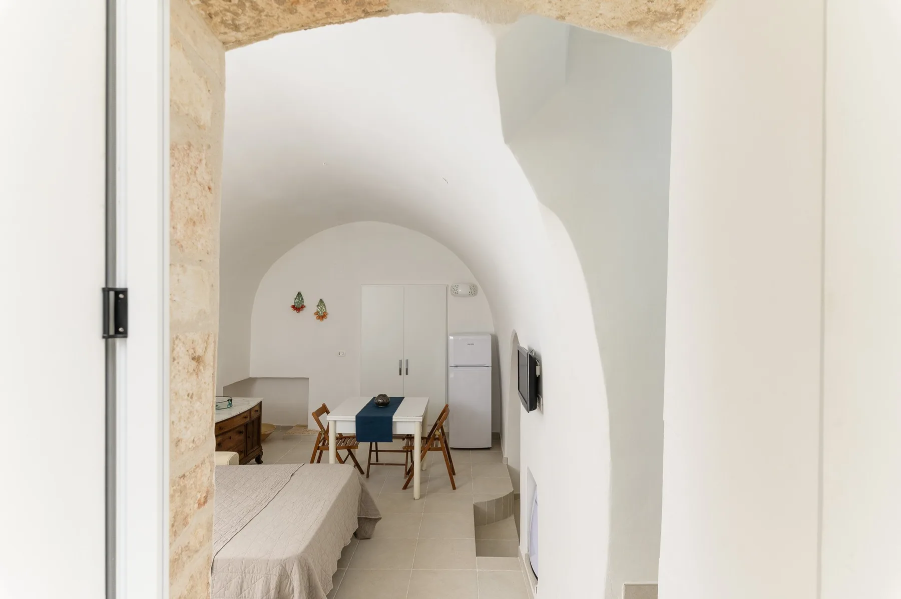 Dormitorio abovedado con una cama, una mesa y un refrigerador.