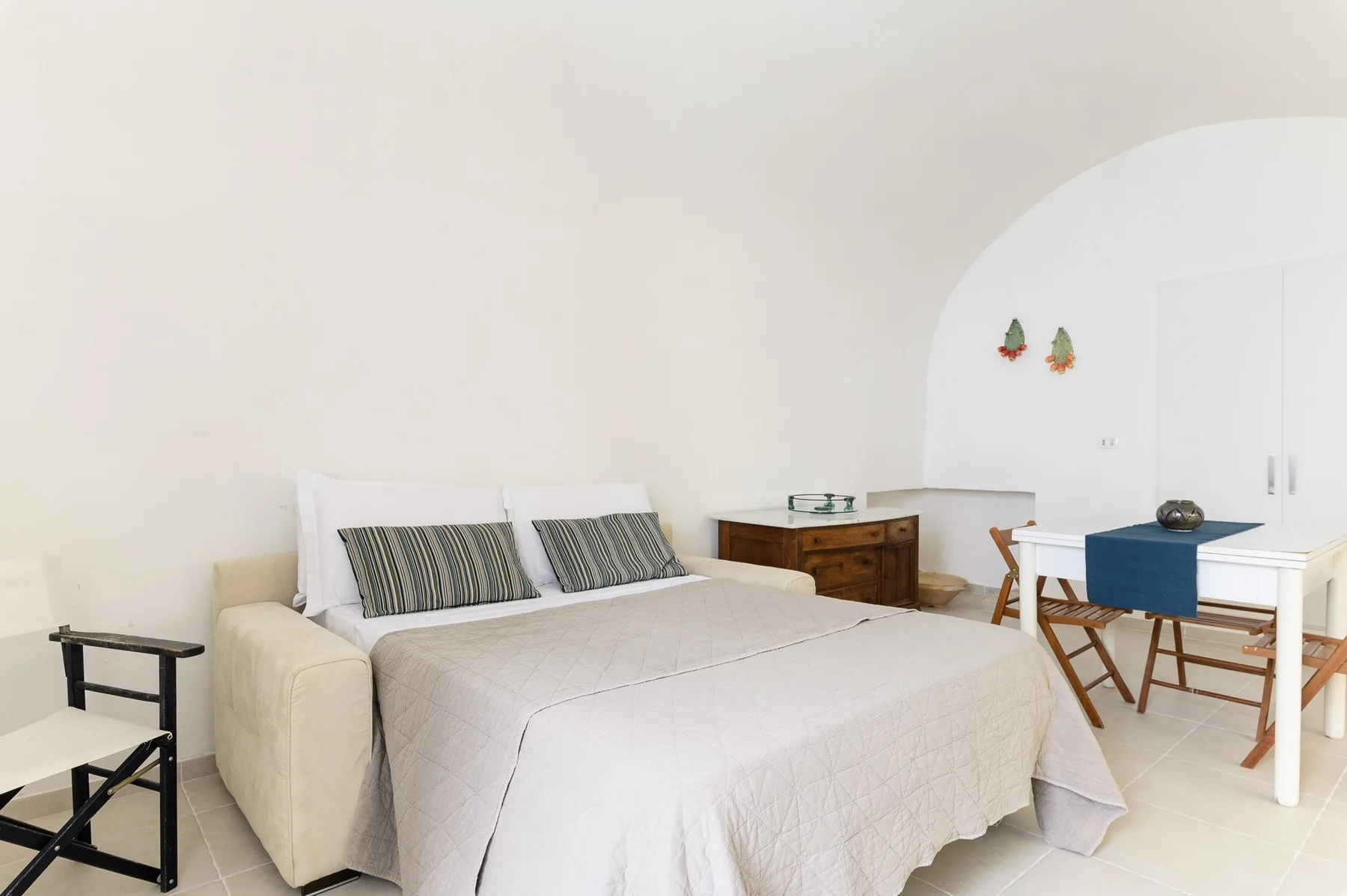 Un dormitorio luminoso tiene una cama, una cómoda de madera y una mesa pequeña.