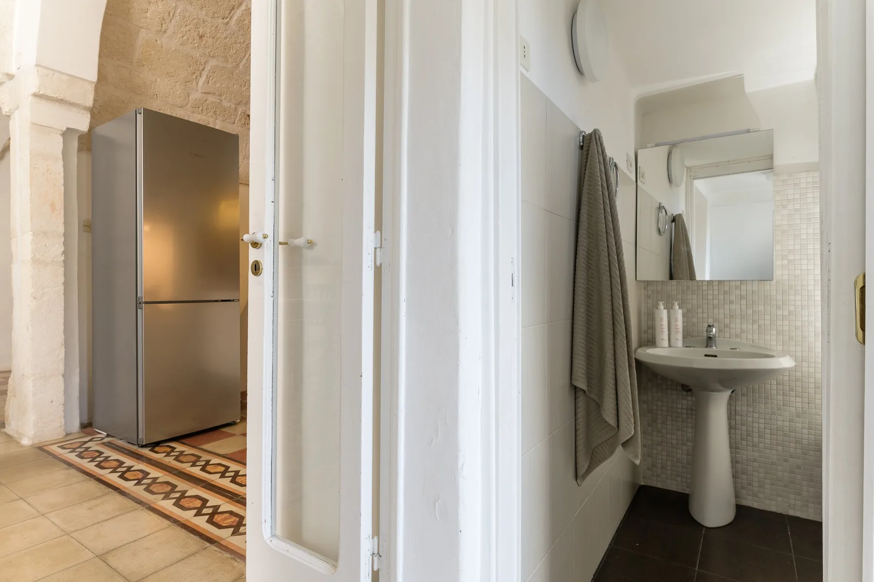 Un baño con lavabo de pedestal, espejo y toalla colgada.