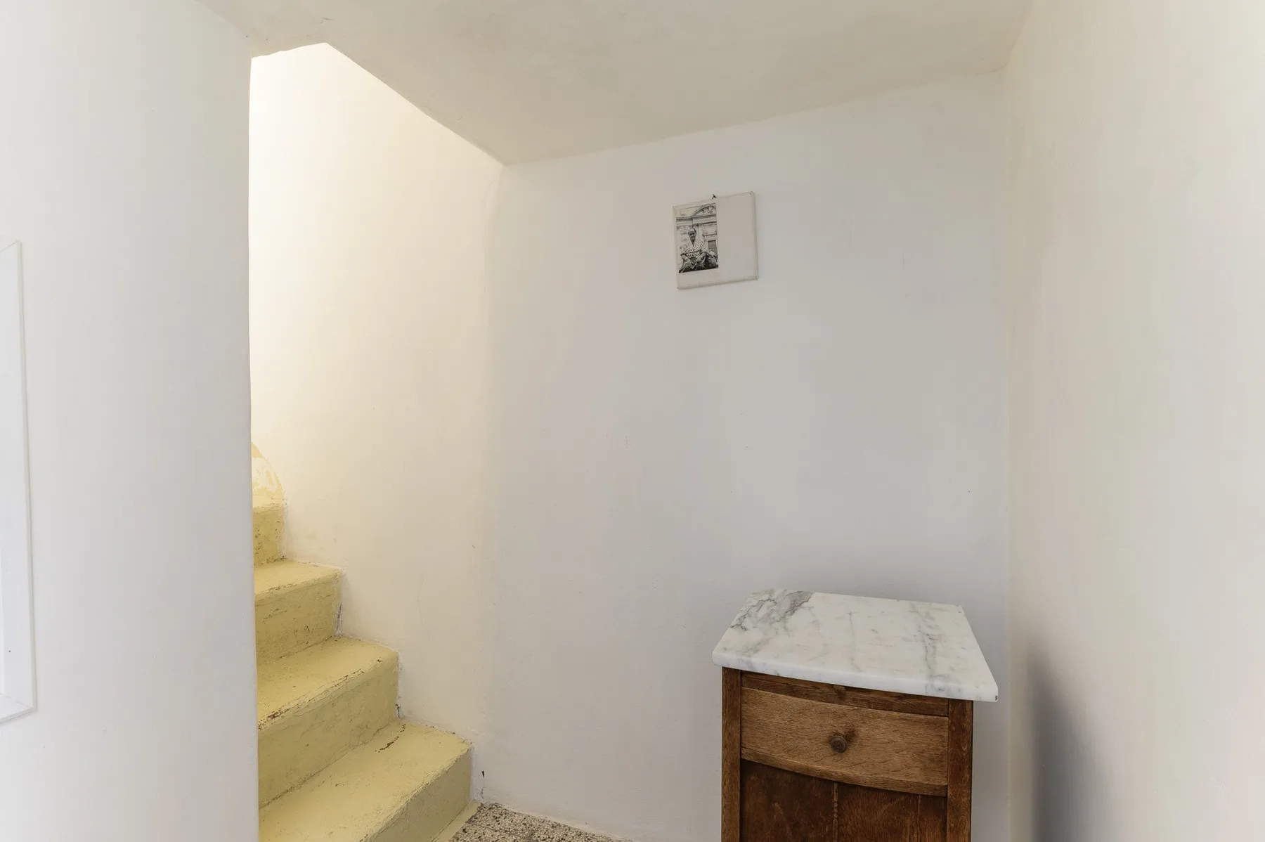 Una pequeña escalera interior junto a un mueble de madera y paredes blancas.