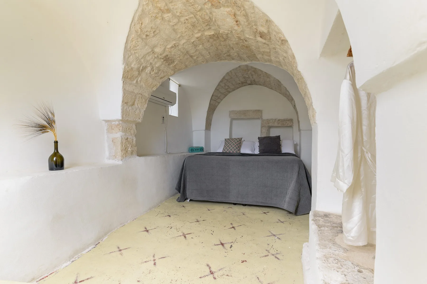 Un dormitorio con una cama bajo techos de piedra abovedados y un suelo claro estampado.