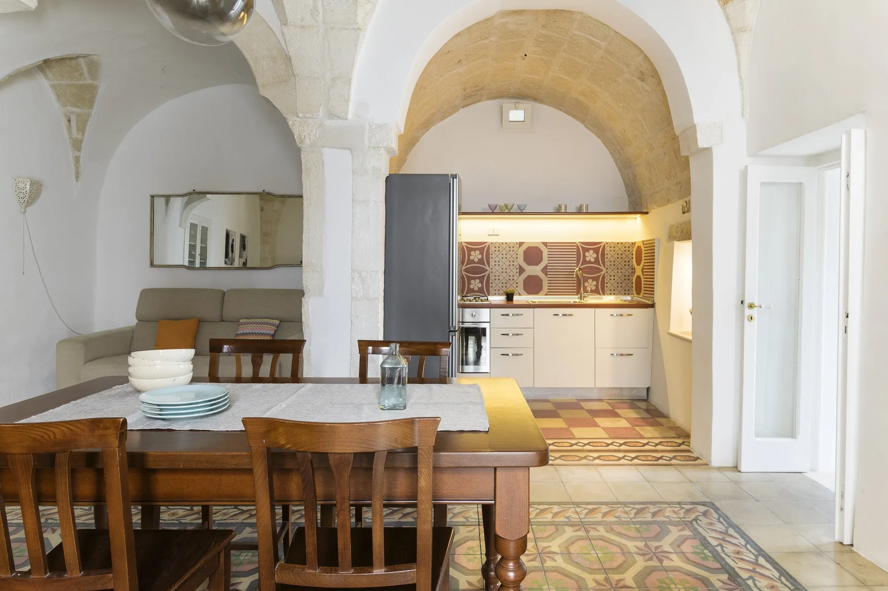 Un comedor se abre a una cocina bajo un amplio arco de piedra.