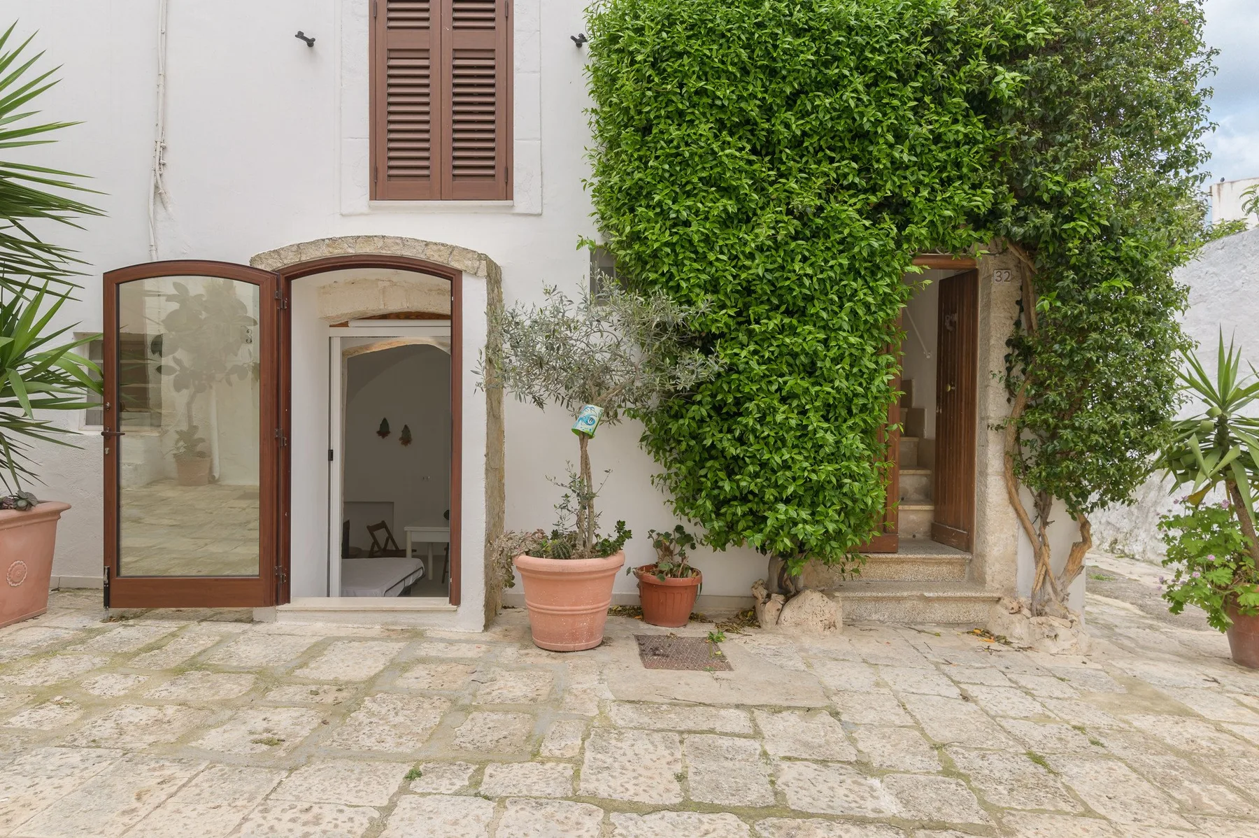 Un patio empedrado con dos puertas abiertas y plantas frondosas.