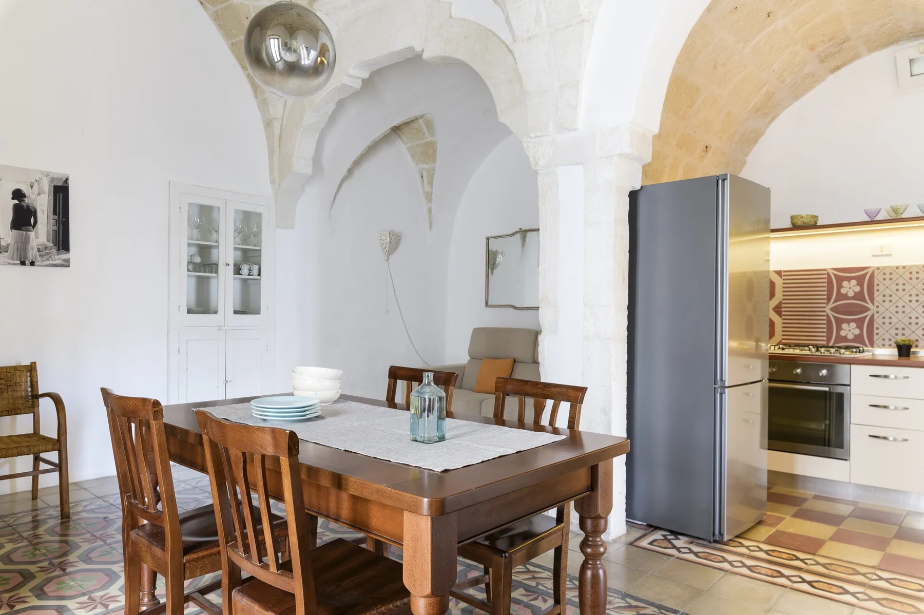 Comedor con una mesa de madera bajo un arco de piedra blanca, junto a una cocina abierta.
