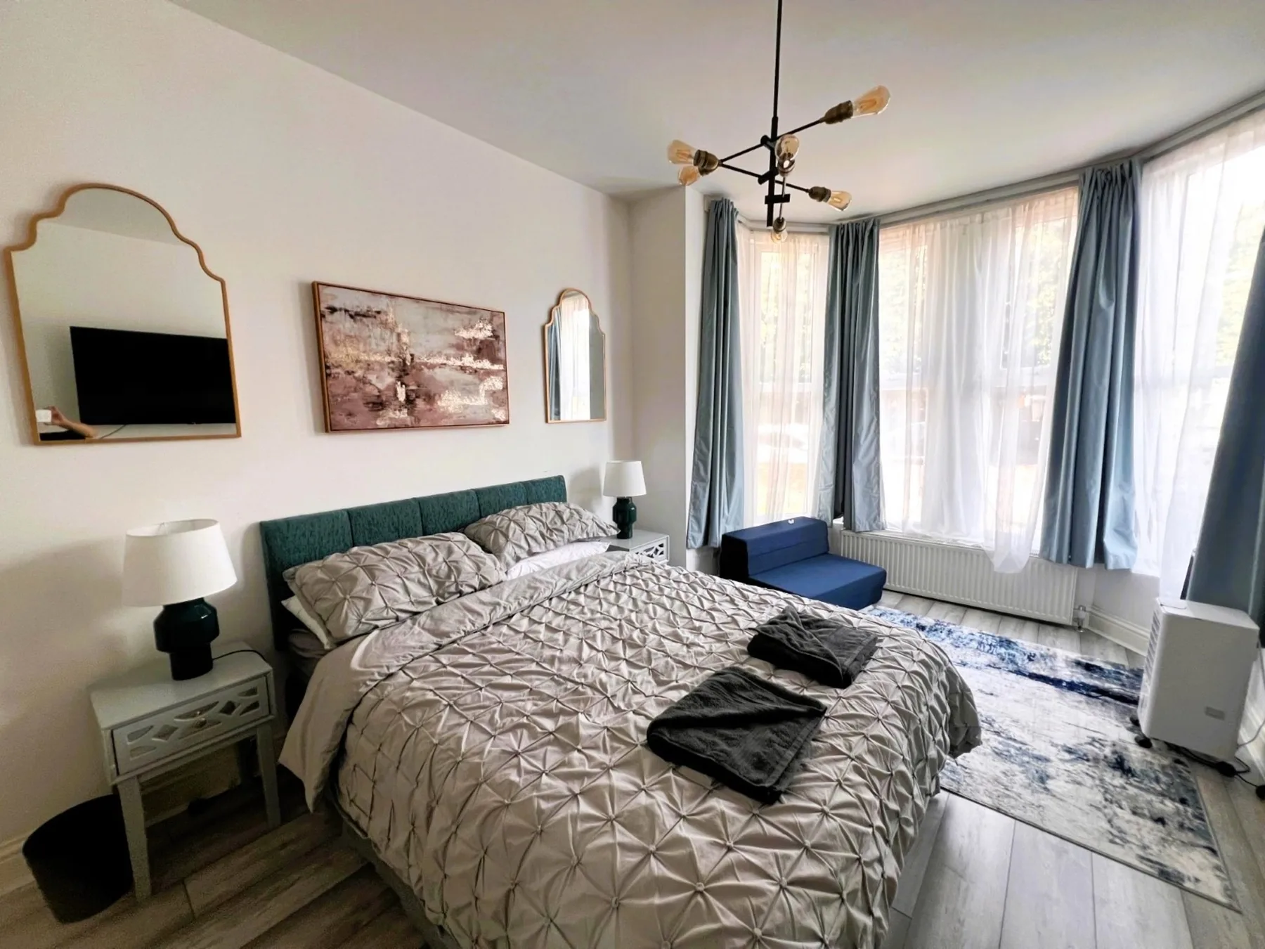 A bedroom with a made bed beside tall windows and curtains.