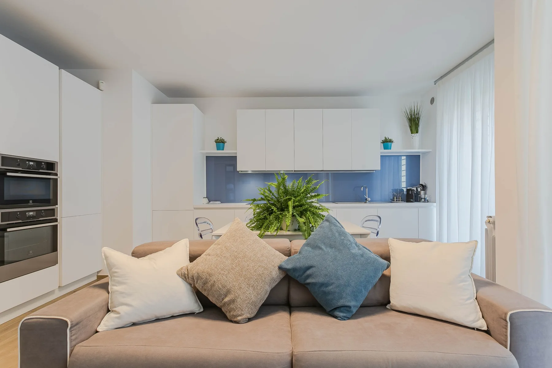 Una sala de estar con un sofá frente a una cocina luminosa.
