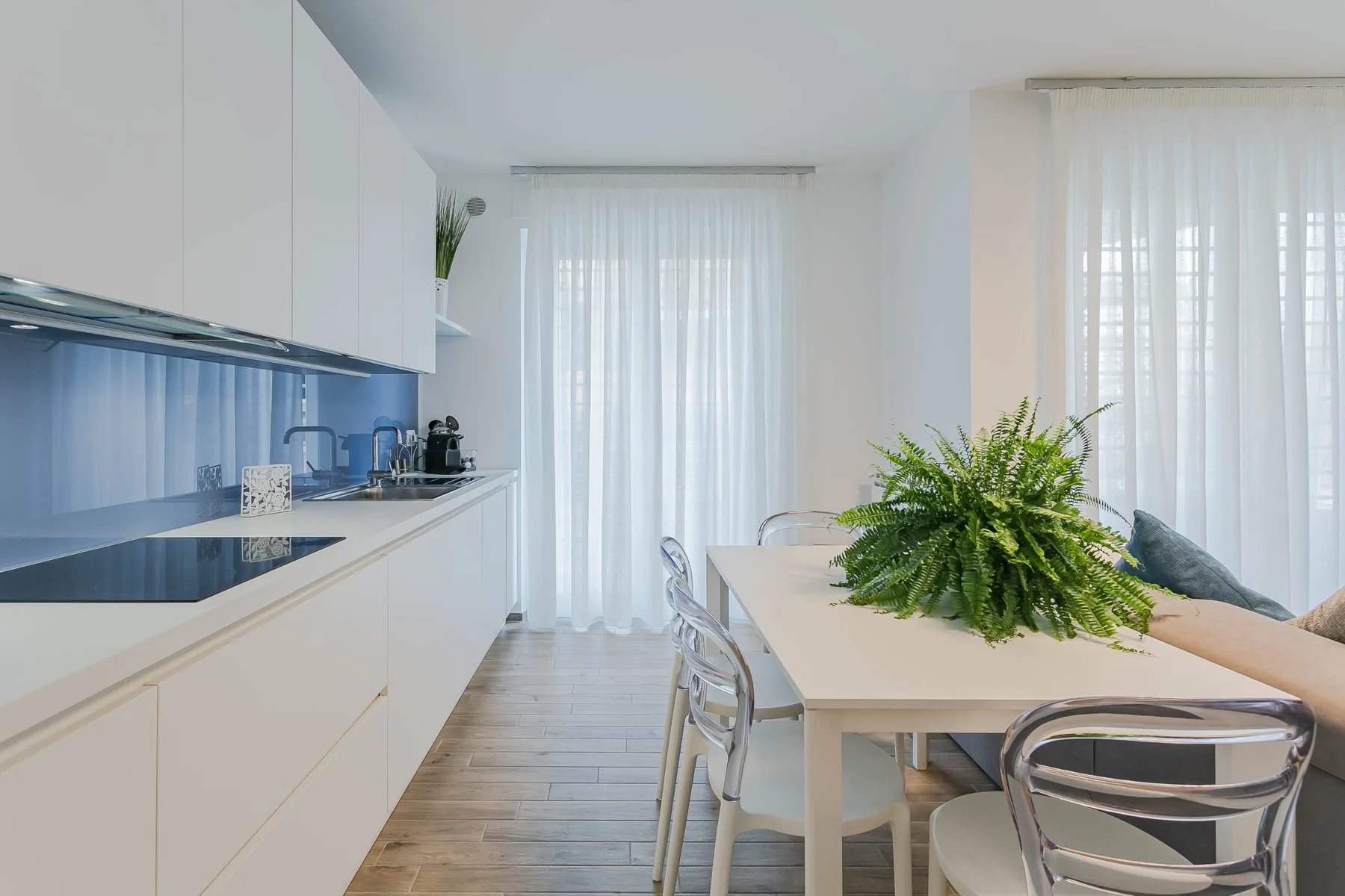 Una luminosa cocina con comedor, muebles blancos, una mesa y un centro de mesa frondoso.