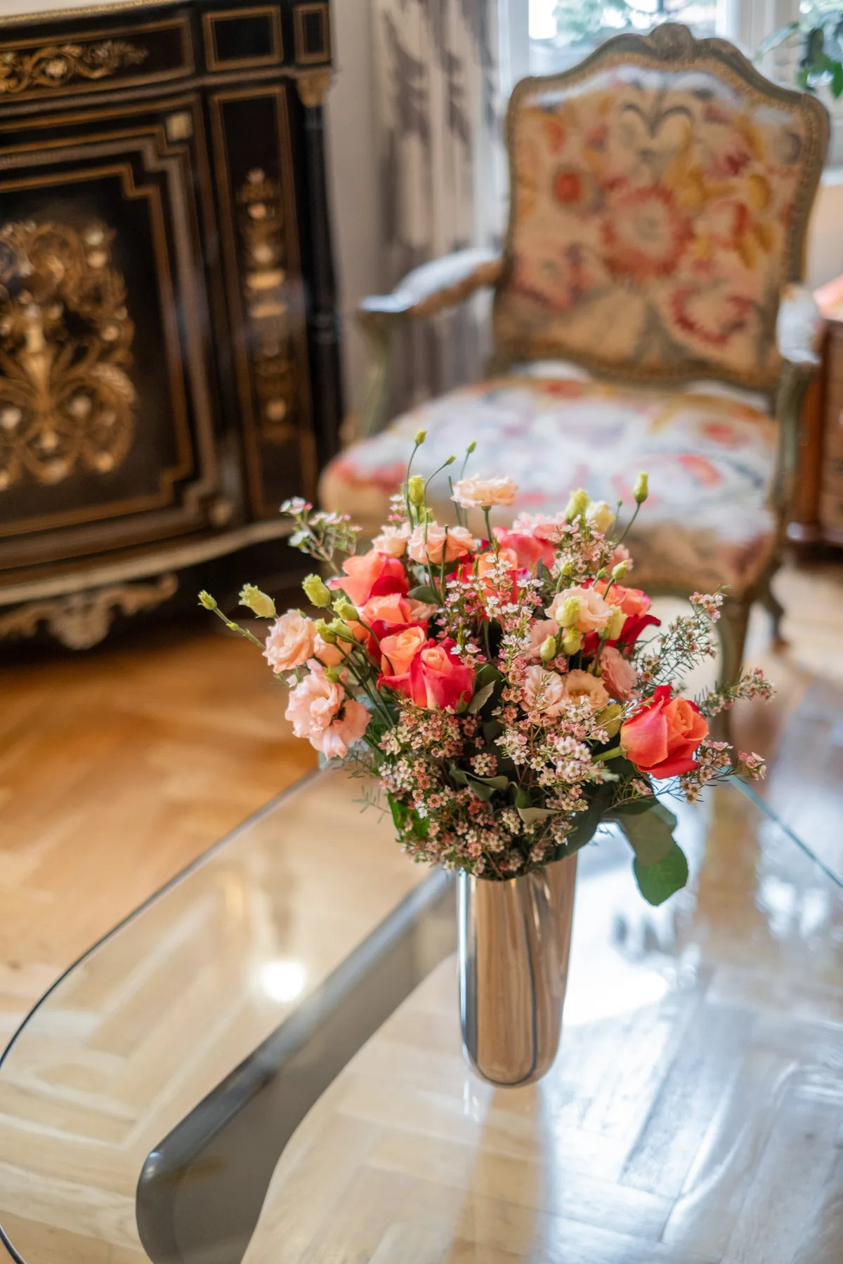 A flower arrangement sits on a glass table in a furnished room.