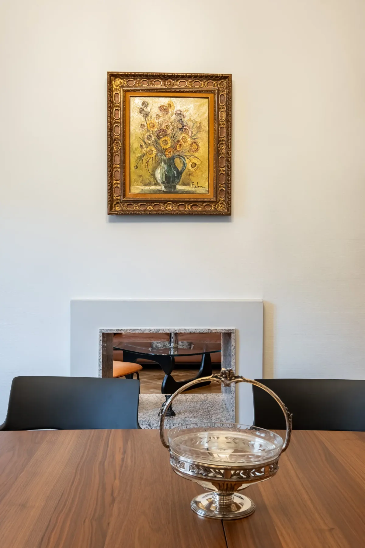 Una mesa de comedor está bajo una pintura floral enmarcada, con un cuenco decorativo de vidrio delante.