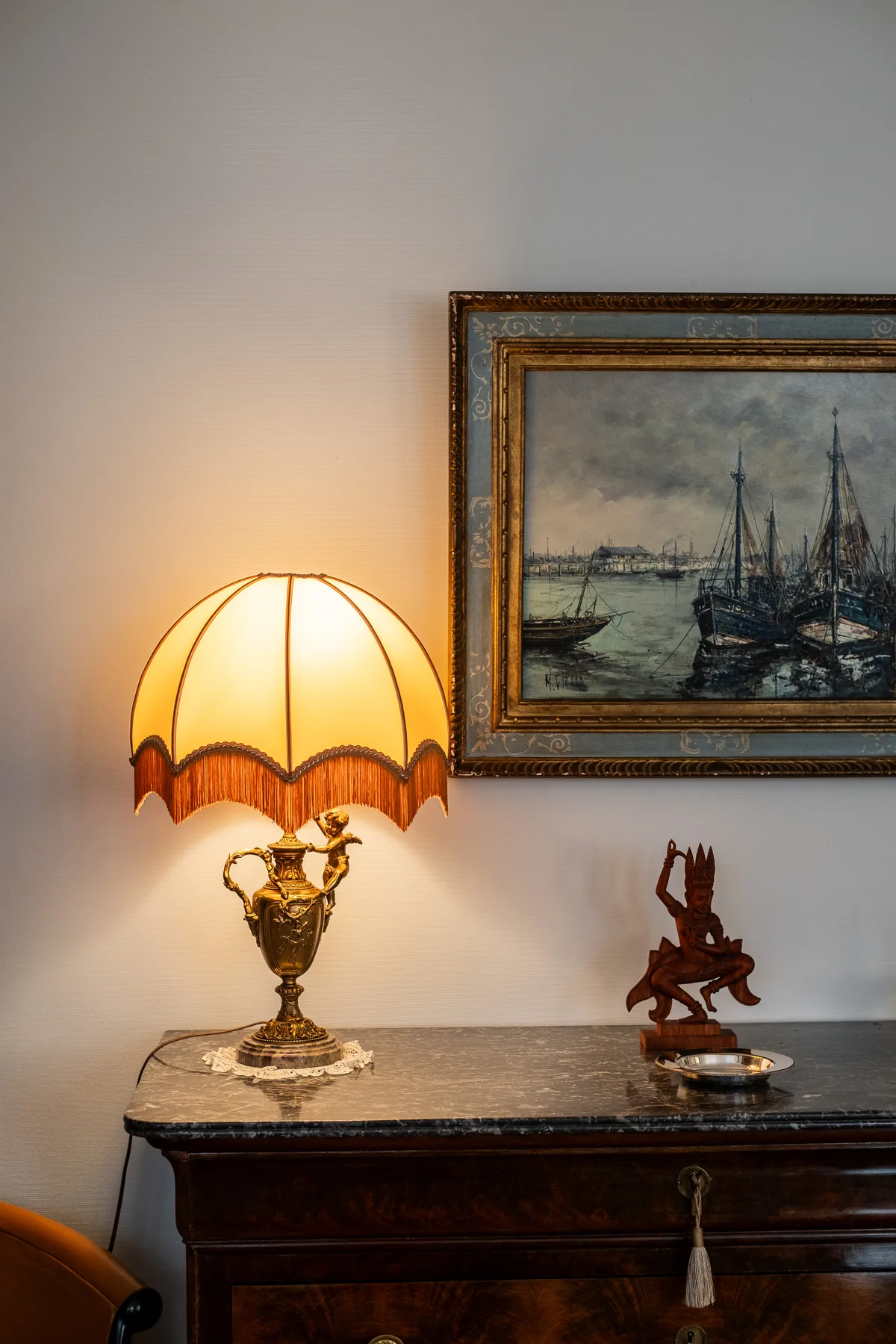 A lit table lamp and framed harbor painting sit above a dark console.