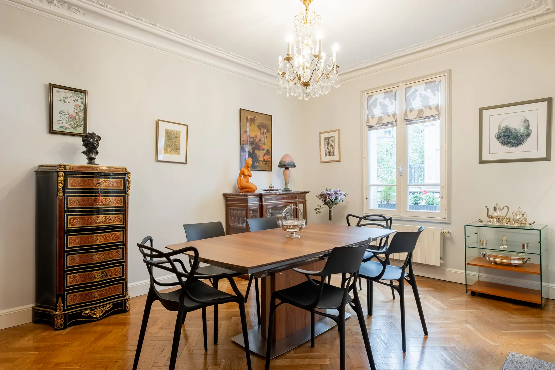 Comedor formal con una mesa de madera, asientos negros y una lámpara de araña.
