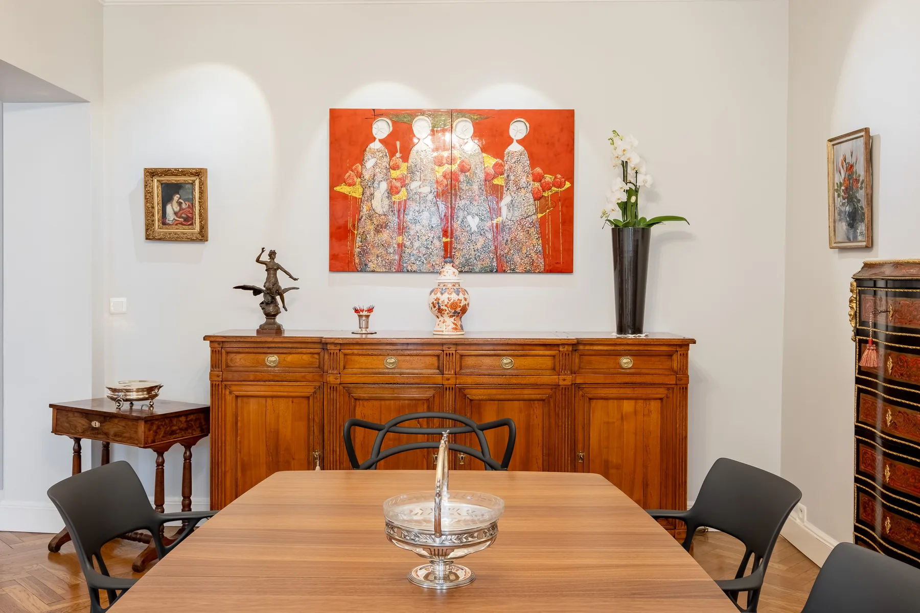 Un comedor con una mesa de madera, un aparador y una obra colorida en la pared.