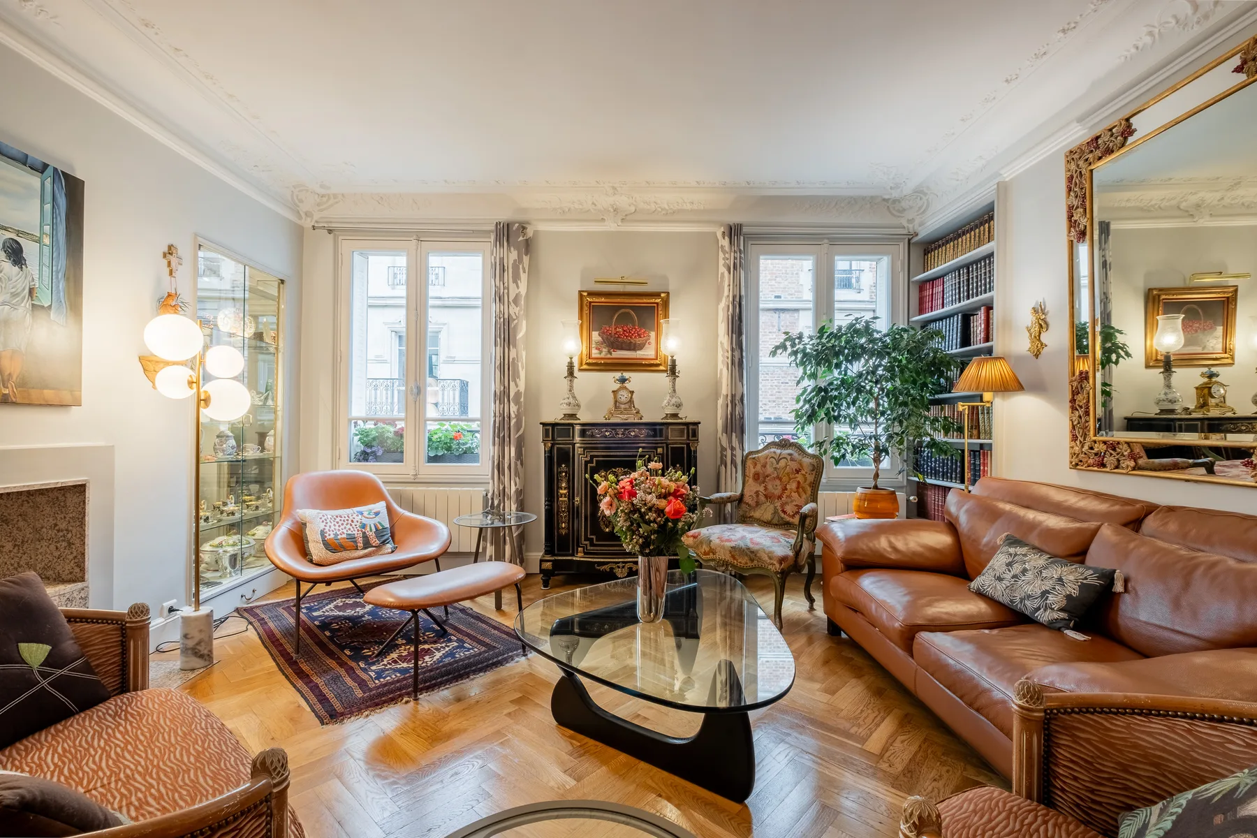 A bright living room with a seating area, glass coffee table, and tall windows.
