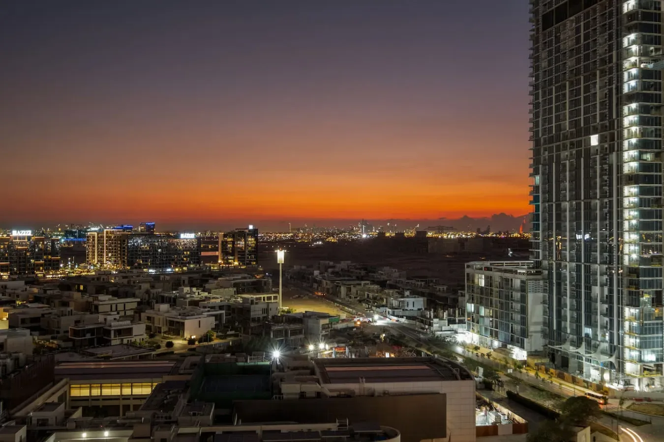 Edificios de la ciudad y una alta torre de vidrio se alzan frente al atardecer.