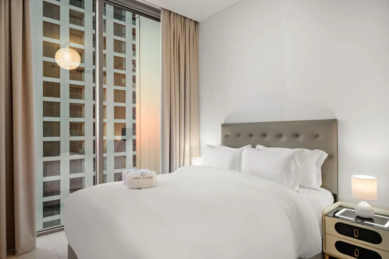Un dormitorio con una cama bien tendida junto a ventanas altas y cortinas.