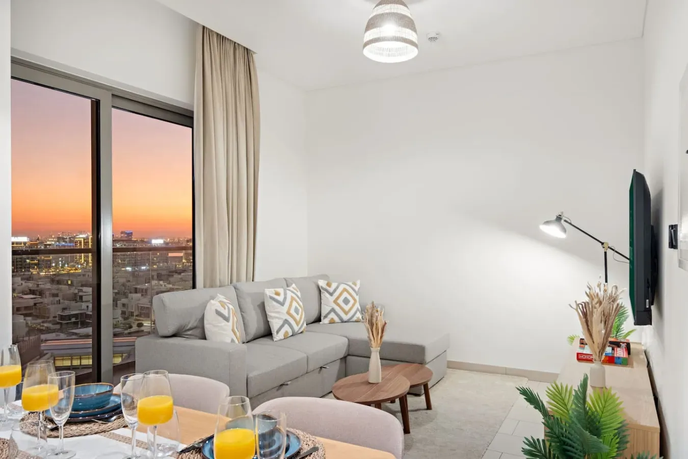 Una sala de estar con asientos, un televisor y una gran ventana con vistas a la ciudad al atardecer.