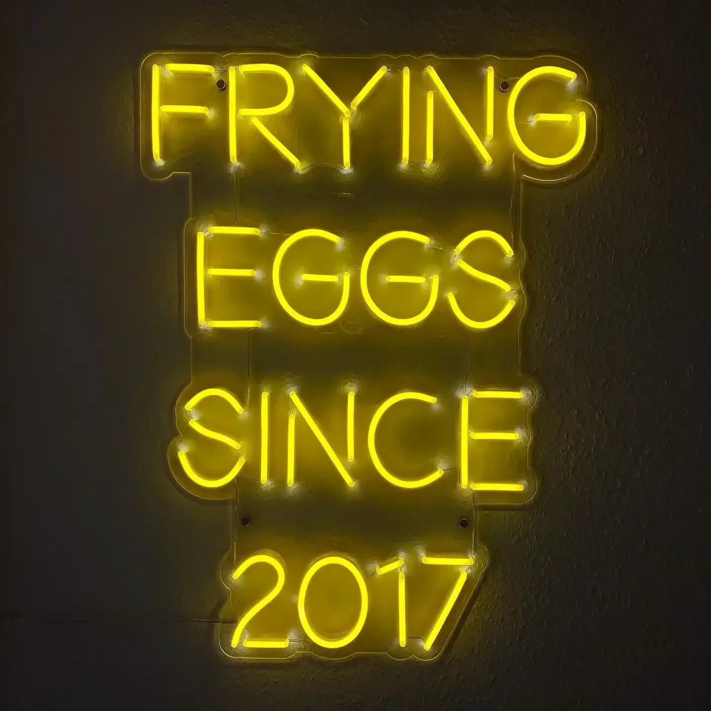 Letrero de neón amarillo que dice «FRIENDO HUEVOS DESDE 2017»